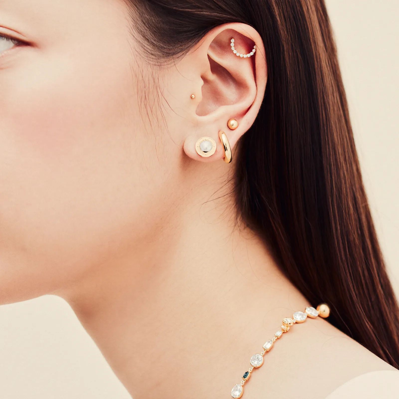 Three-quarter view of a curated ear stack with mixed gold studs and a beaded conch hoop