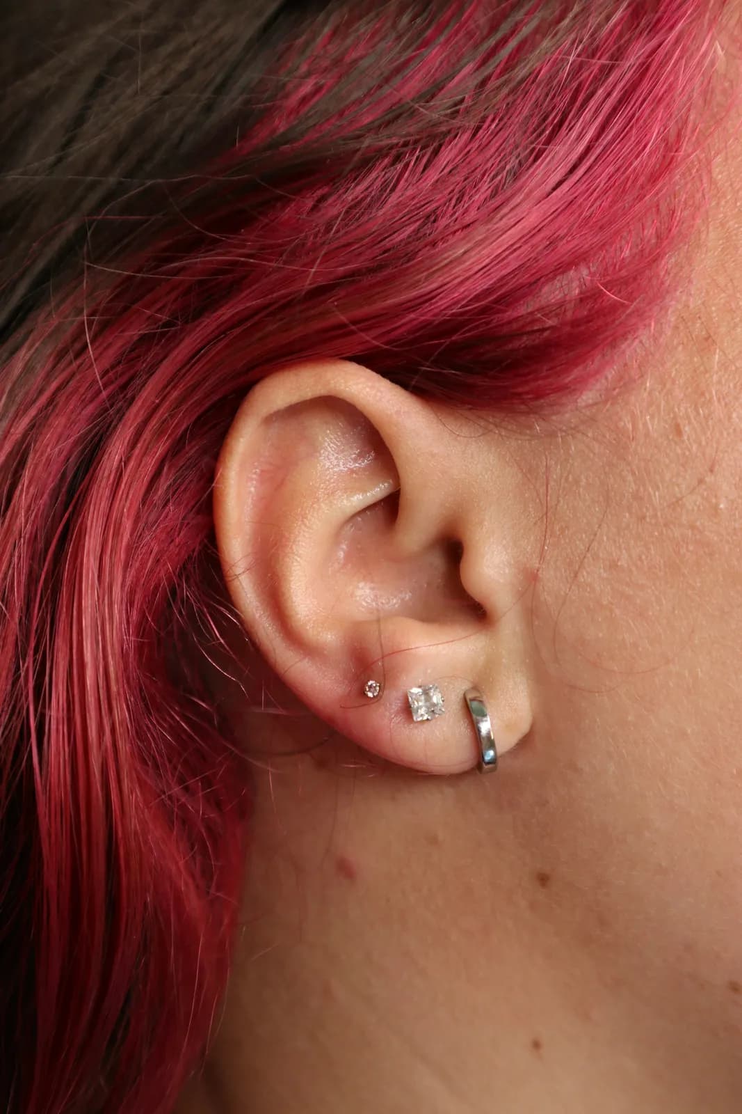 Three lobe piercings — a small prong-set CZ, a princess-cut CZ and a plain seamless hoop
