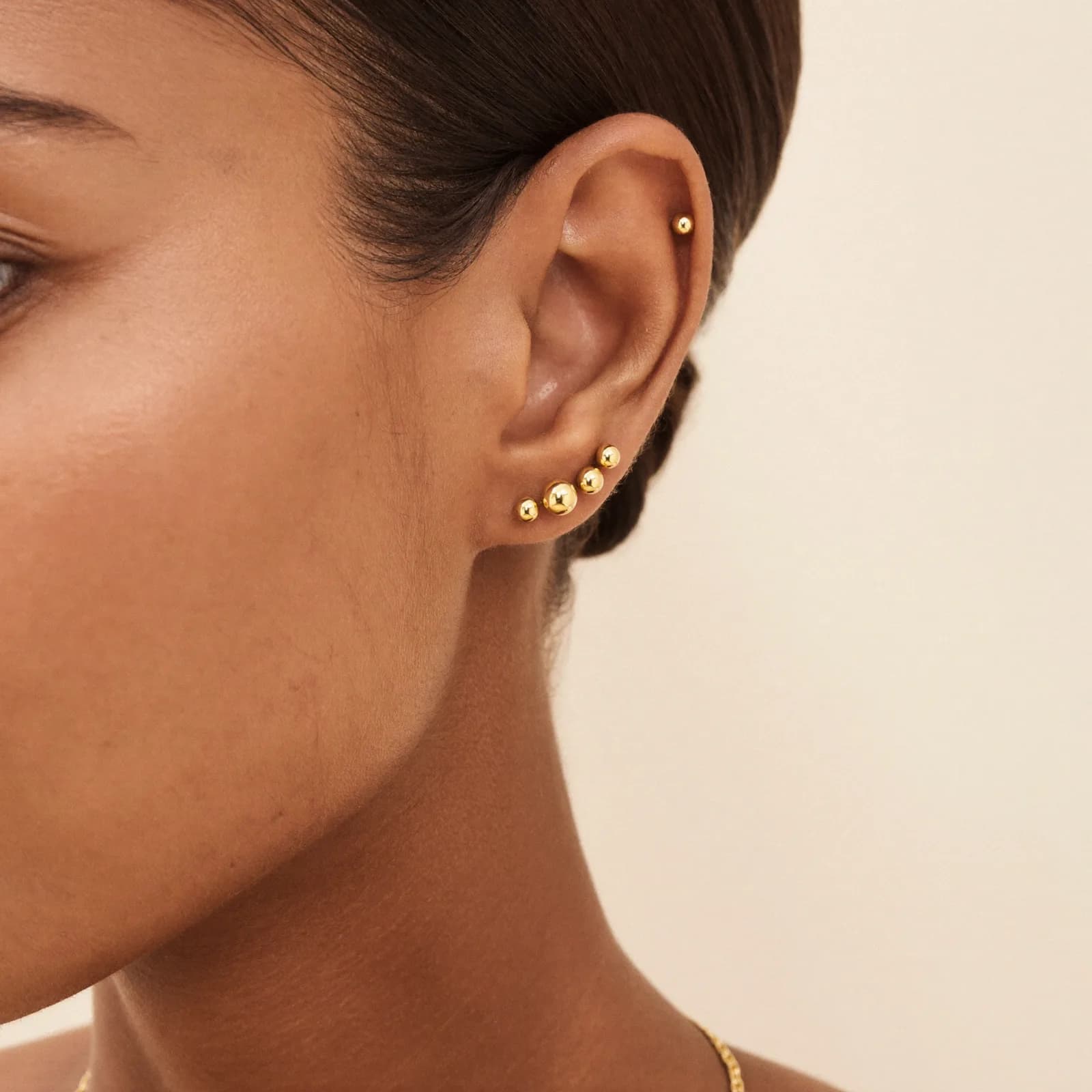 Earlobe with three gold ball studs in a curved line