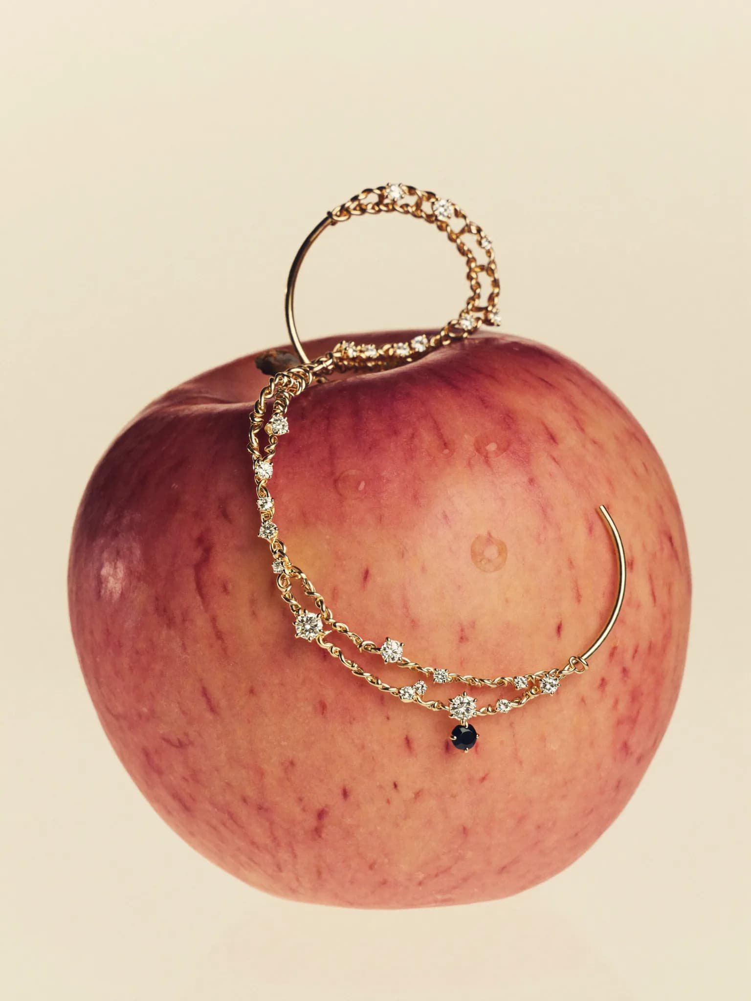 Delicate gold hoop and diamond studs pierced through a pale pink apple