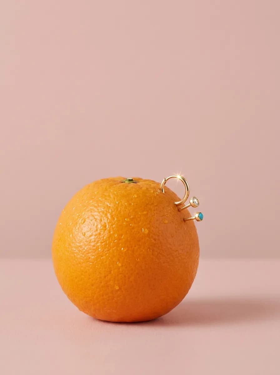 Fine gold piercing jewelry pierced through the rind of a fresh orange